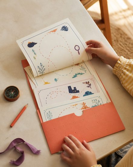 Child opening an illustrated treasure-hunt folder at home
